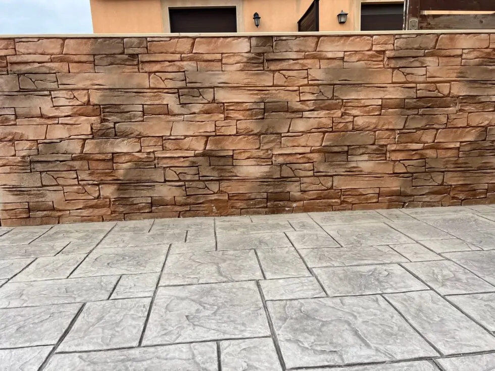 Muro exterior de jardín revestido con hormigón impreso vertical imitación piedra rústica en tonos ocres.